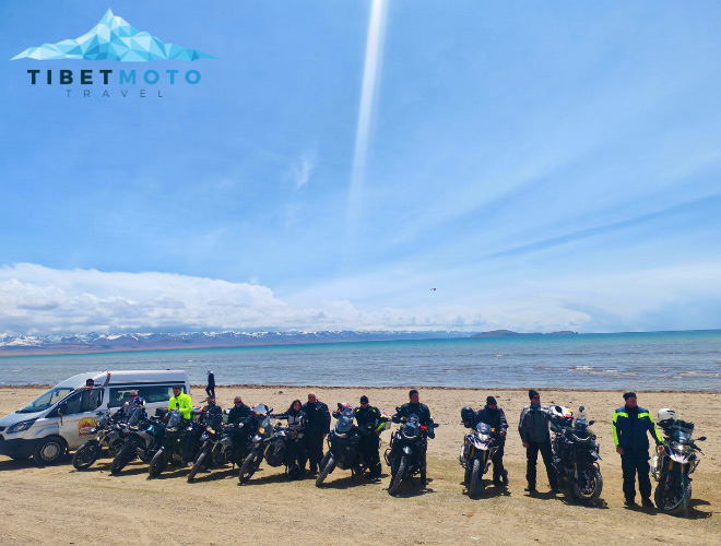 Group photo in front of a lake in Tibet Several motorcyclists pose for a group photo on the shore of a lake in Tibet. The lake stretches to the horizon, with snow-covered mountains rising in the background.