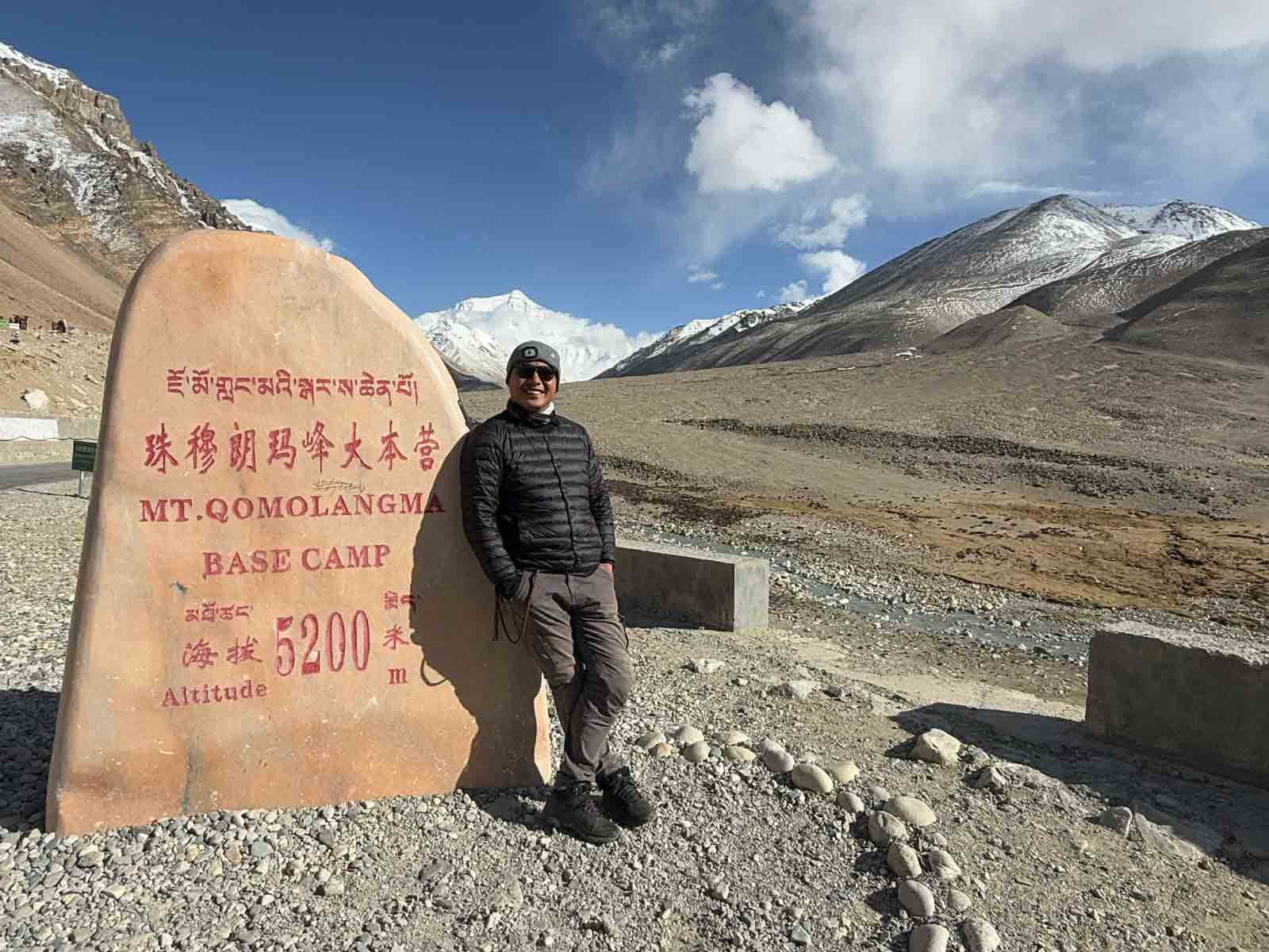 traveler at mount everest base camp monument tibet Traveler standing beside the Everest Base Camp monument at 5,200 meters with Mount Everest visible in the distance.